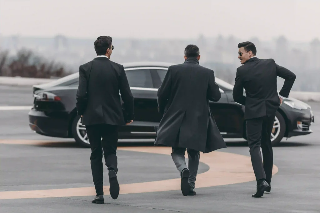 Three businessmen in suits walk towards a luxury black car on a foggy day. Experience premium Black Car Service Annapolis for executive travel.