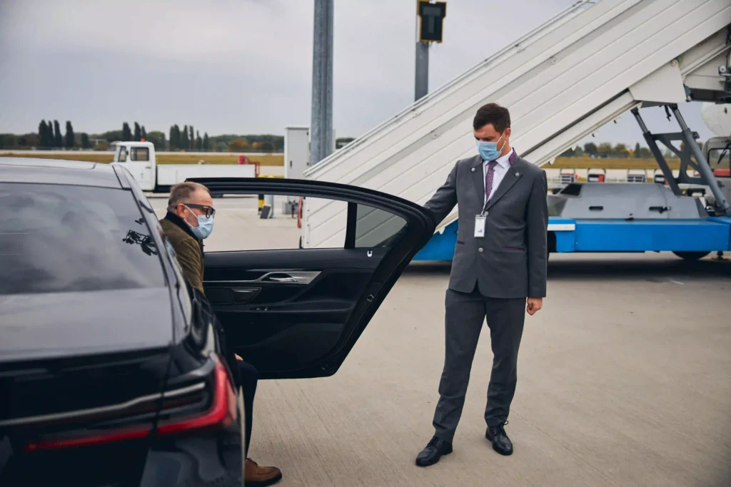 Luxury airport transfer with Black Car Service Annapolis. A chauffeur in a suit opens the door for a masked passenger arriving at the terminal.